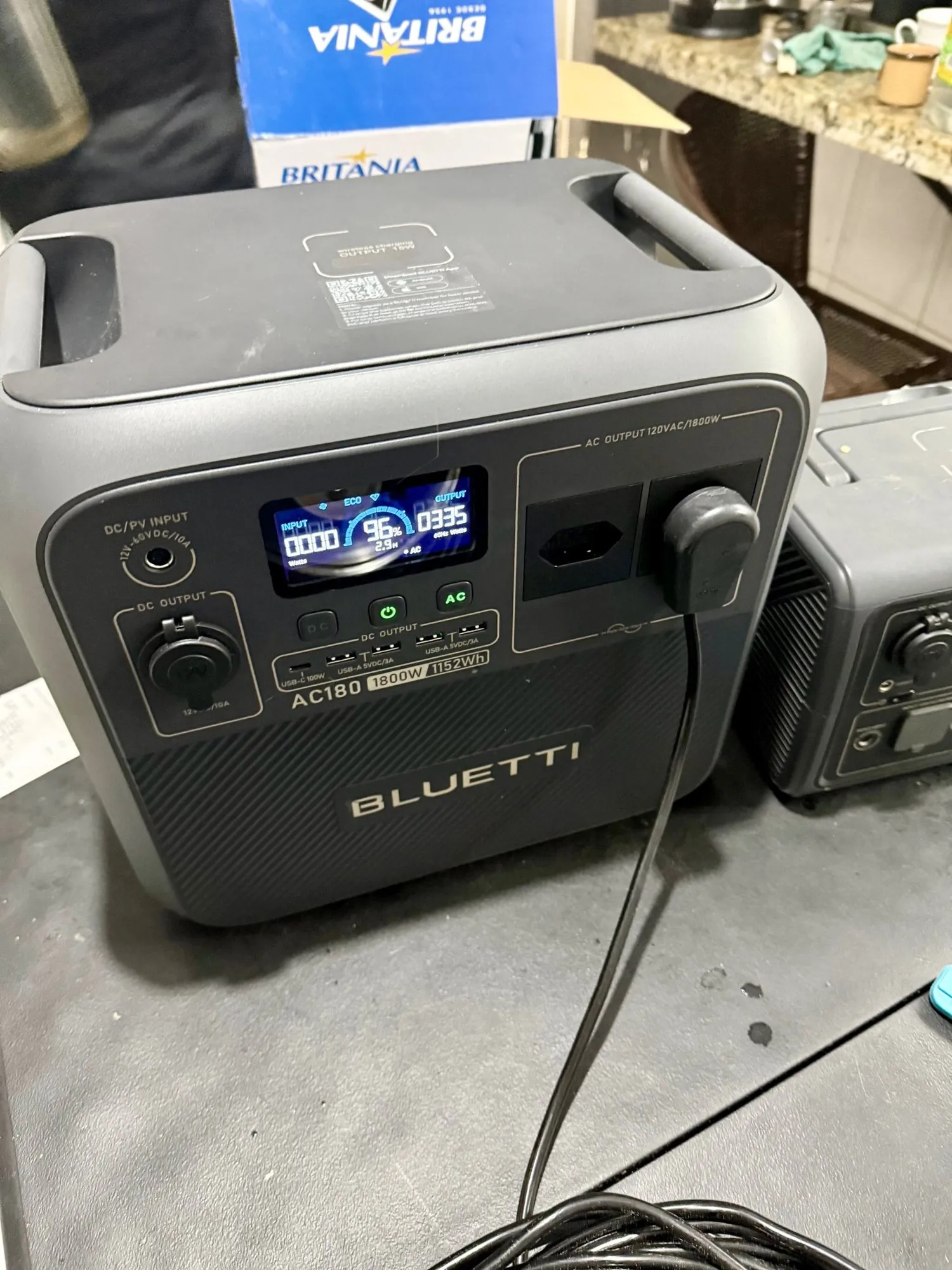 Bluetti AC180 ligada em uma tomada, ao lado de outra estação de energia